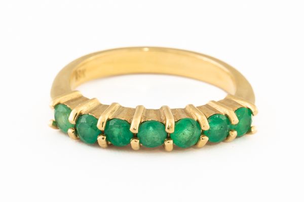 A GOLD AND EMERALD SEVEN STONE HALF HOOP RING