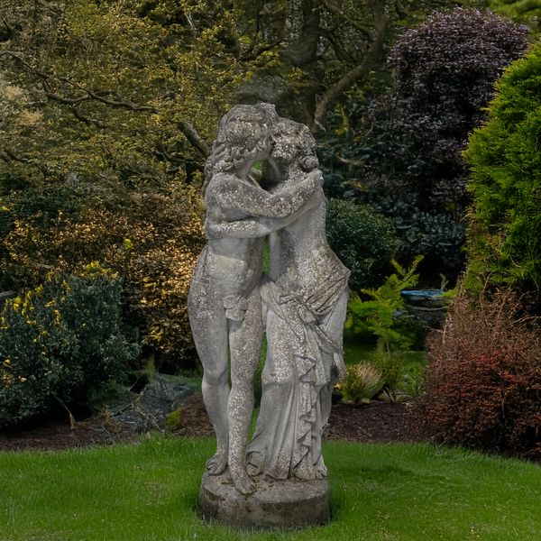 A RECONSTITUTED STONE FIGURE GROUP MODELLED AS A SCANTILY CLAD EMBRACING COUPLE