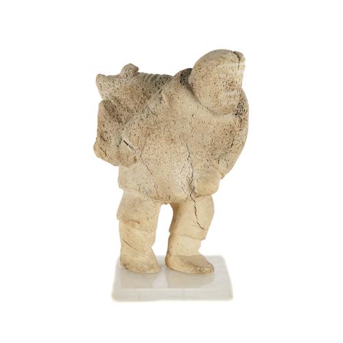 AN INUIT WHALEBONE CARVED FIGURE OF A MAN CARRYING A SACK