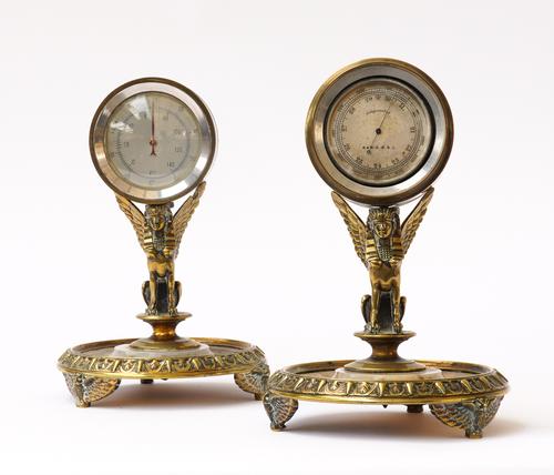 OF EYGPTOMANIA INTEREST: A PAIR OF GILT-BRASS AND ONYX MOUNTED WINGED SPHNIX DESK STANDS FITTED WITH A THERMOMETER AND BAROMETER (2)