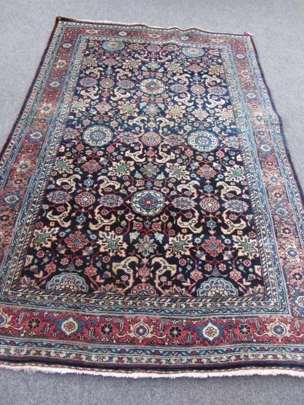 A Sarough rug, Persian, the indigo field with an allover design of flowerheads, vines and floral sprays, with a madder palmette border, 228cm x 144cm.