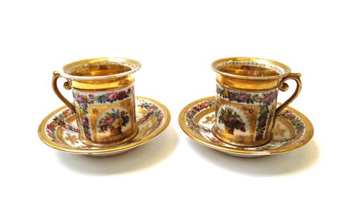 A pair of Paris porcelain cabinet cups and saucers, early 19th century, painted with baskets of flowers inside gilt frames against a ground filled wit