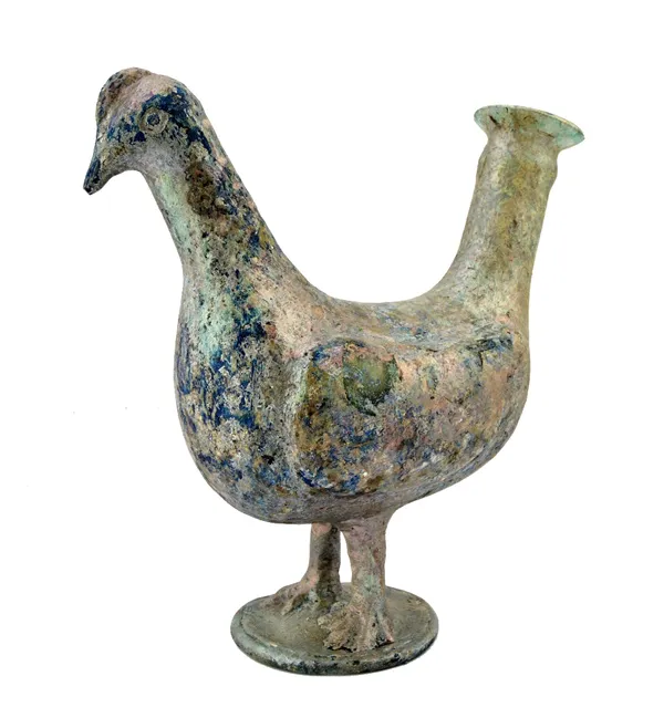An Islamic glass bird vessel, possibly Raqqa, 12th century or later, standing on a circular base, its tail forming the spout, 24cm. high.   Illustrate