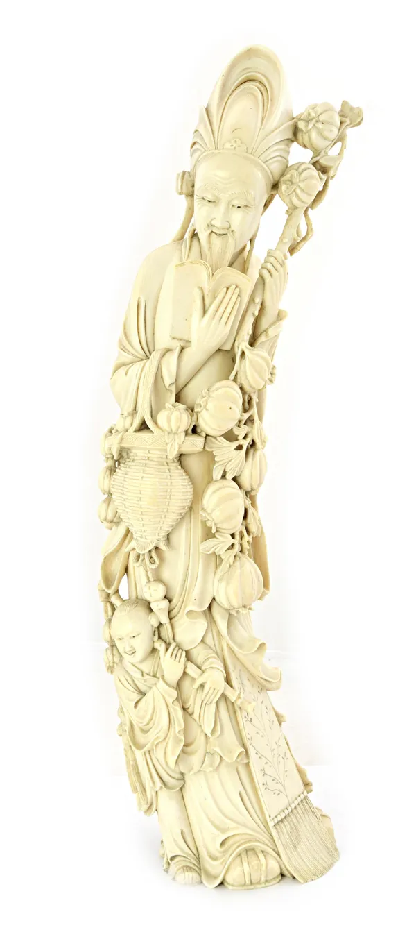 A tall Chinese ivory carving, early 20th century, depicting a bearded man reading a book and carrying a basket of fruit and a branch laden with fruit,