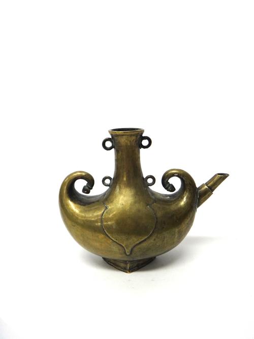An Islamic bronze spouted vessel, probably late 19th century, with crescent shaped body and curled finials, the neck applied with four rings, 25cm. hi
