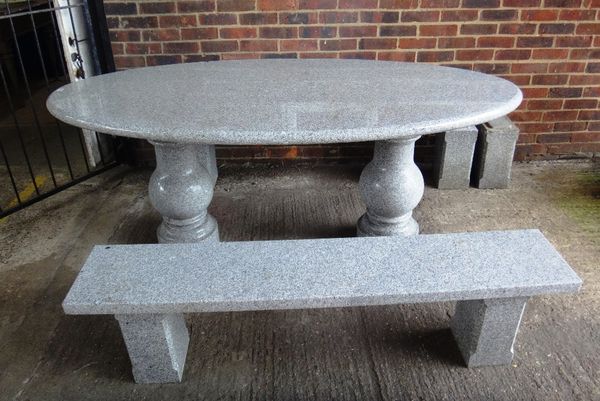 A 20th century carved granite oval table on turned baluster supports, 200cm wide, together with a pair of rectangular benches, each 160cm wide. (3)