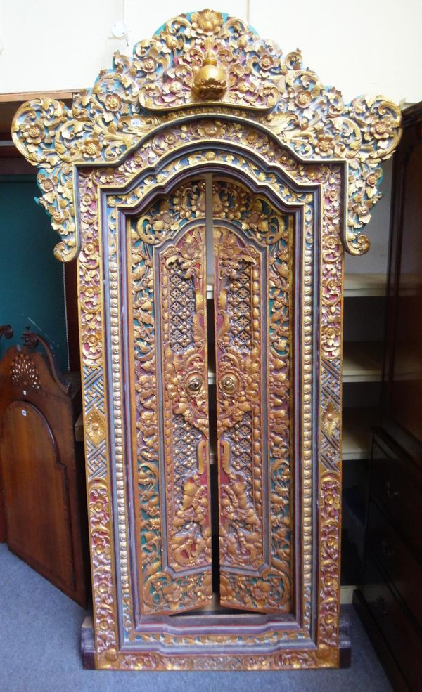 A 20th century profusely carved, painted and gilded Tibetan door and frame, with stepped arch top crest and a pair of doors, 132cm wide x 235cm high.