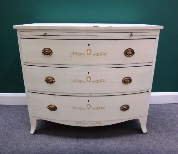 An early 19th century and later parcel gilt white painted bowfront chest, with brushing slide over three long graduated drawers and splayed bracket fe