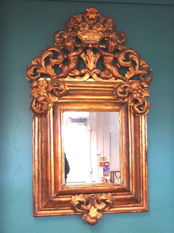 An 18th century gilt framed wall mirror, the upper crest relief carved with cherubs holding flowering baskets, over a cushion framed rectangular mirro