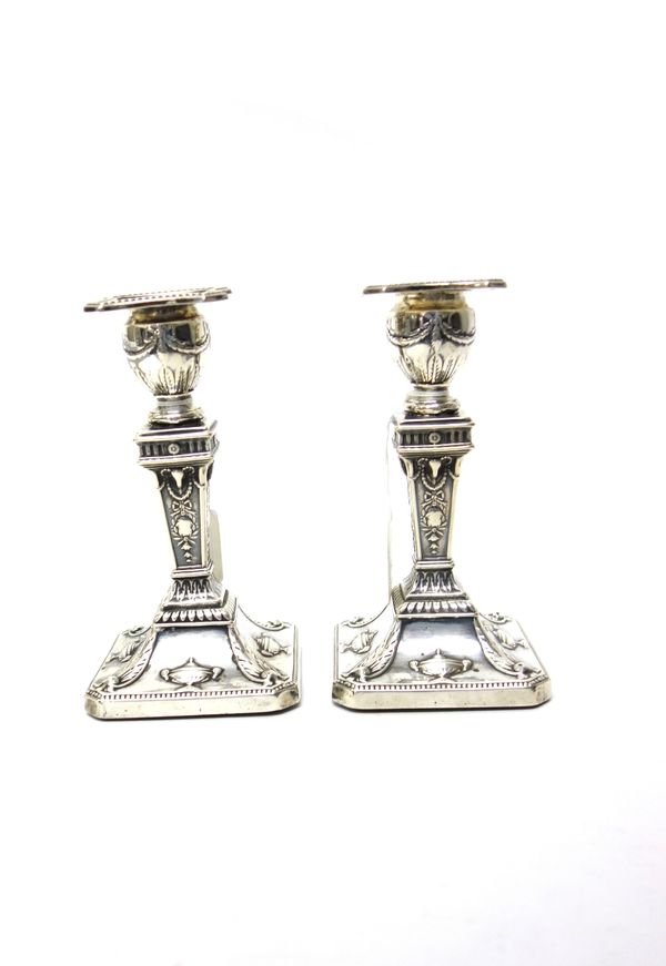 A pair of late Victorian silver table candlesticks, each with a tapering square column, decorated with ram's heads and on a swept cut cornered square