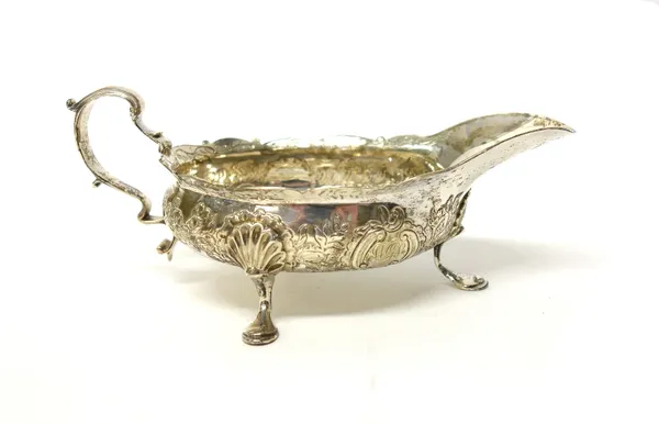 A George III Scottish silver sauceboat, with a shaped rim, scrolling handle and raised on three shell capped feet, the body having later decoration, E