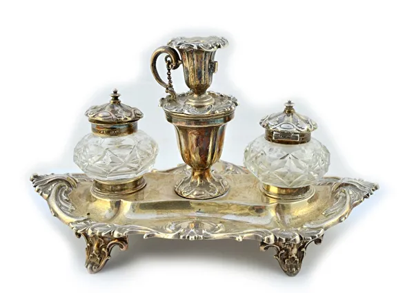 A Victorian silver twin bottle inkstand, of shaped oval form, having a scroll decorated rim, raised on four feet, the centre fitted with a taperstick