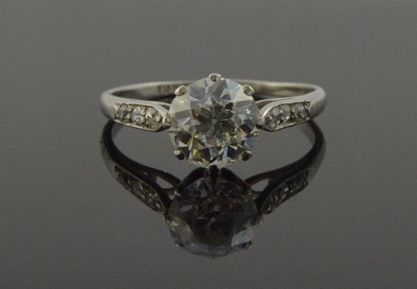 A platinum and diamond set ring, claw set with the principal cushion shaped diamond at the centre, between diamond set three stone shoulders, detailed