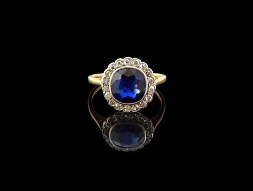 A gold, sapphire and diamond set cluster ring, mounted with the cushion shaped sapphire at the centre, within a surround of small cushion shaped diamo