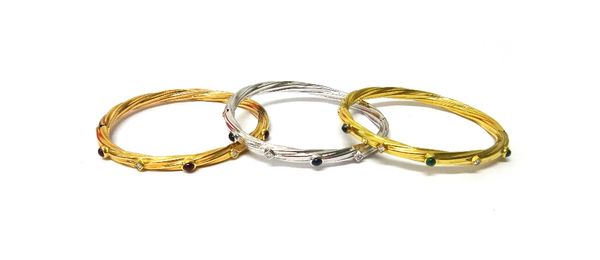 A set of three, three colour gold and gemstone set oval hinged bangles, comprising; a white gold, diamond and cabochon sapphire set bangle, in a ropet