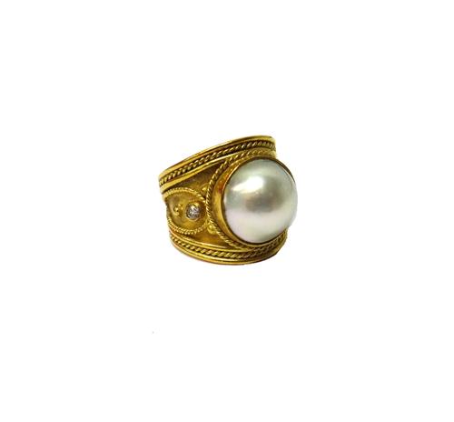 A gold, diamond and mabe pearl set ring, mounted with the large mabe pearl at the centre, between two circular cut diamonds, the mount in a Hellenisti