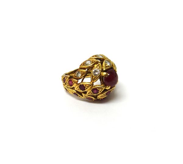 An 18ct gold, ruby and diamond set ring, in a bombe and pierced foliate design, mounted with a circular cabochon ruby at the centre and otherwise set