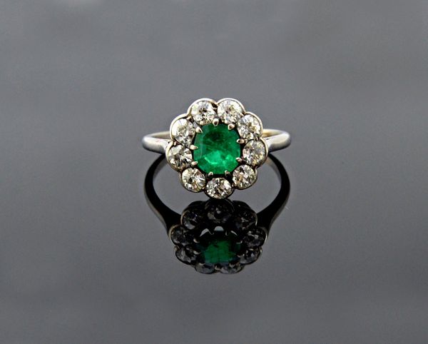 A platinum, emerald and diamond set cluster ring, claw set with the step cut emerald at the centre, in a surround of nine cushion shaped diamonds, rin