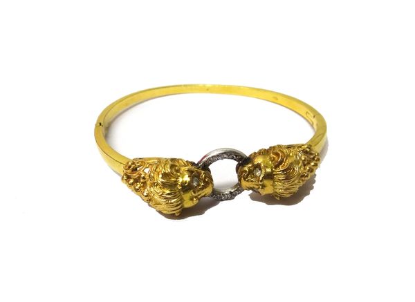 A gold and diamond set oval hinged bangle, the front formed as two facing lion's masks, with diamond set eyes, connected by a circular loop, mounted w