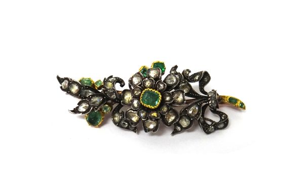 An emerald and diamond set brooch, designed as a floral and foliate spray, with a ribbon twist terminal, mounted with foil backed emeralds and with fo