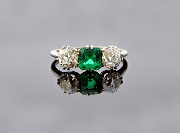 A diamond and emerald set three stone ring, claw set with the cut cornered square cut emerald at the centre, between two cushion shaped diamonds, ring