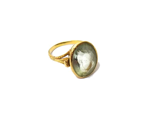 A gold ring, collet set with an oval cut pale light green aquamarine, between feathered shoulders, ring size R and a half.