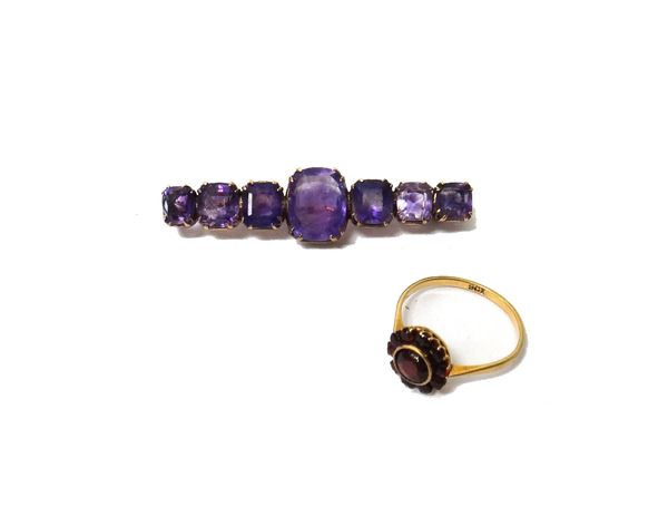 A gold and amethyst set seven stone bar brooch, mounted with a row of cushion shaped amethysts, graduating in size to the centre stone and a gold and