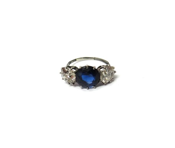 A diamond and synthetic sapphire set three stone ring, claw set with the circular cut synthetic sapphire at the centre, between an old-cut and a brill