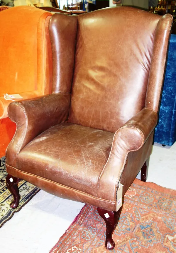 A mahogany brown leather wing armchair.