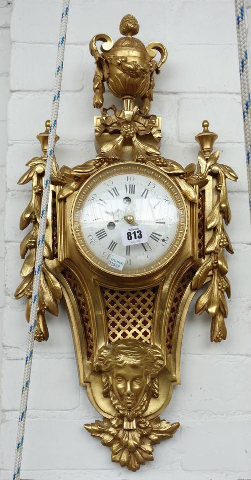 A gilt bronze Cartel clock, early 20th century, with urn finial over a white enamel dial flanked by foliate swags, with pierced grille and mask embell