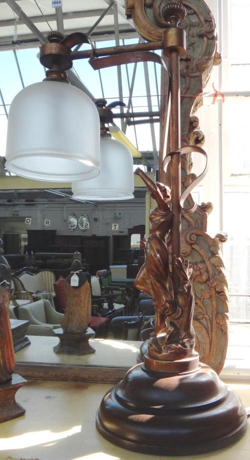 A patinated spelter figural table lamp of Art Nouveau style modelled and cast as a maiden beneath a hanging frosted shade on a turned oak base, 85cm h