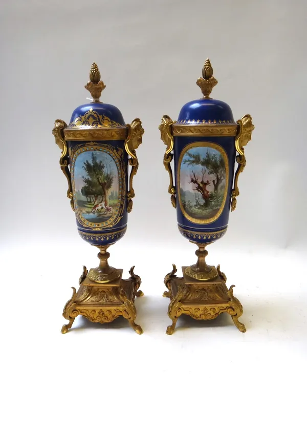 A pair of Sevres style gilt metal mounted two handled vases and fixed covers, late 19th century, painted with rural scenes against a gilt blue ground