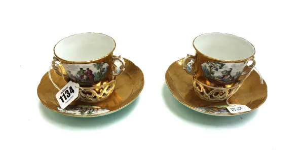 Two Berlin porcelain trembleuese two handled cups and saucers, late 19th century, each decorated with cartouches of hunting scenes against a gilt grou