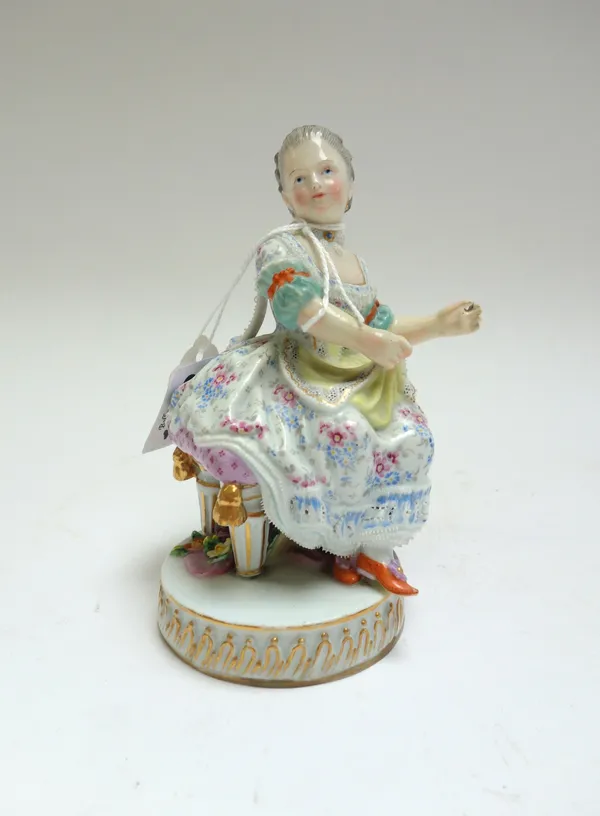 A Meissen porcelain figure, late 19th century, modelled as a lady in a floral dress, seated on a circular gilt base, with blue crossed sword and incis