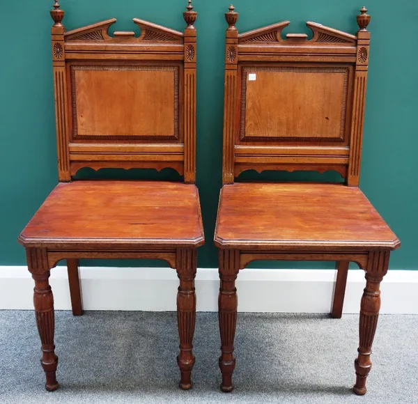 A pair of Victorian mahogany hall chairs, with broken architectural crest, panel back and solid seat, on reeded supports, (2).