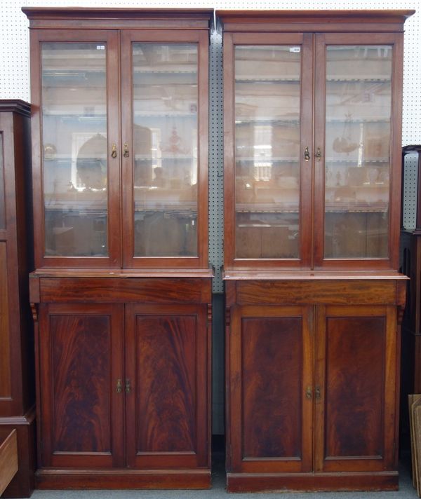 A pair of 19th century mahogany bookcases, each with a pair of glazed doors enclosing shelves revealing hidden compartments behind, over flush fit dra