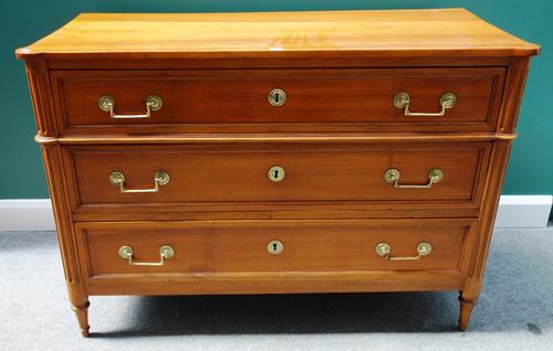 An early 19th century French walnut three drawer commode with fluted rounded corners on tapering turned supports, 132cm wide.