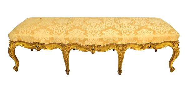 A large 19th century Italian gilt framed rectangular footstool, with carved three quarter frieze on eight scroll supports, 185cm wide.  Illustrated