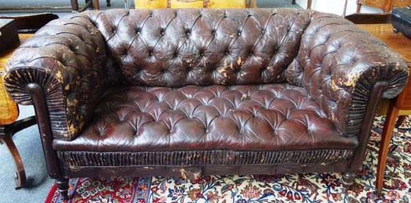 An early 20th century button back rouge leather upholstered Chesterfield three piece suite, to comprise a sofa and a pair of tub chairs, on turned sta