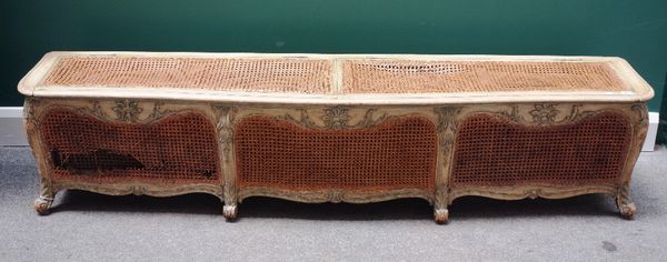 A 19th century French polychrome painted large foot stool, with lift up serpentine top and bergere panels on leaf scroll feet, 186cm wide.