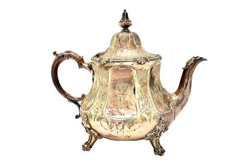 A Victorian silver teapot, of compressed pear shaped form, having a scrolling handle and raised on four shaped feet, otherwise with engraved decoratio
