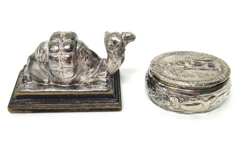 A silver model of a resting camel, on an ebonised rectangular stand, London 1904 and a silver oval hinge lidded box, with embossed decoration, the cov