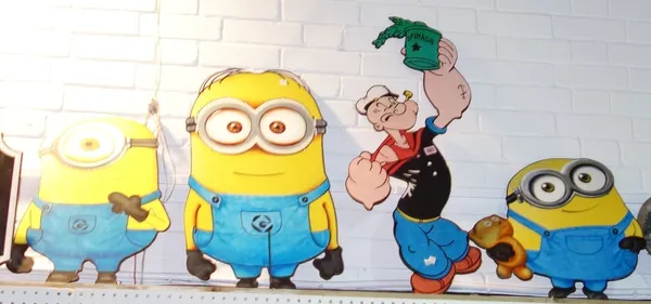 A group of three fret cut wooden panels painted with 'minions' and another painted with Popeye.