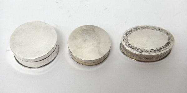 A George III silver oval pill box, decorated with engraved borders, Birmingham 1799 and two silver plain circular pill boxes and covers, (3).