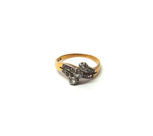 A gold and diamond set ring, claw set with a row of three cushion shaped diamonds, in a cross over design, between rose diamond set two row shoulders,