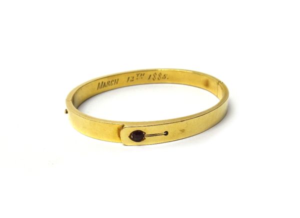 A Victorian gold and garnet set oval hinged bangle, in a strap design, mounted with a cushion shaped garnet, detailed March 12th 1885, gross weight 12