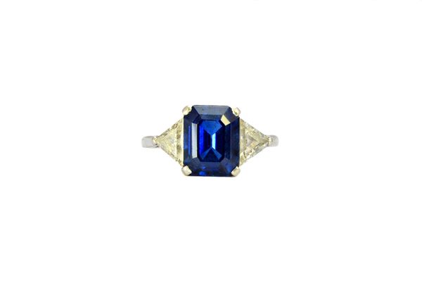 A sapphire and diamond set three stone ring, claw set with the cut cornered rectangular emerald cut sapphire at the centre, between two triangular cut