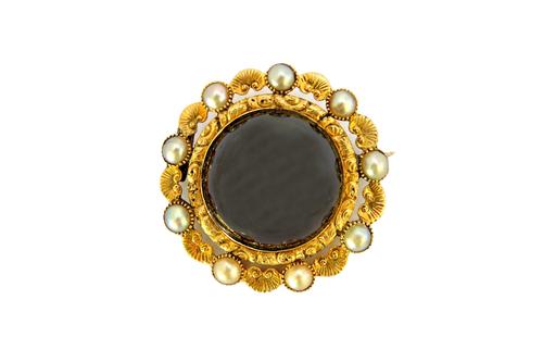 A Victorian cabochon garnet and half pearl set brooch in a circular scrolling and foliate setting, gross weight 15.4 gms, with a case.  Illustrated