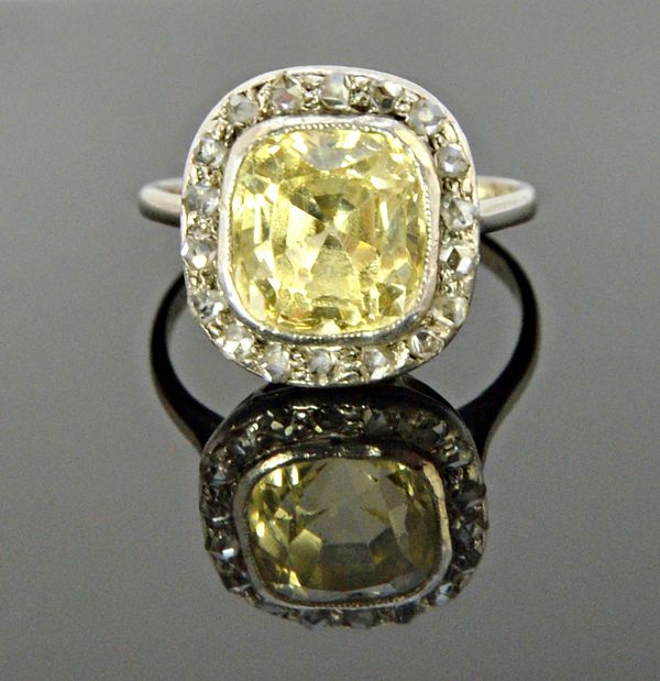 A yellow sapphire and diamond set cluster ring, mounted with the cushion shaped pale yellow sapphire at the centre, within a surround of rose cut diam