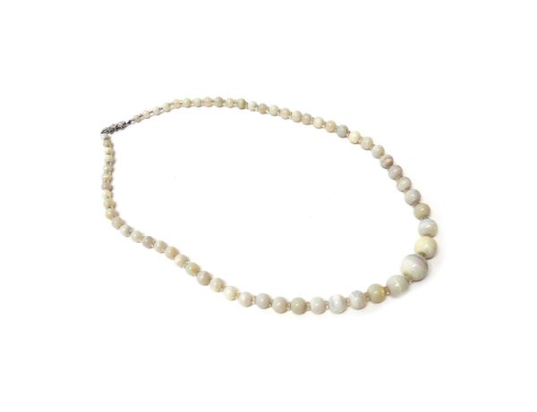 A single row necklace of graduated opal beads, with faceted crystal divisions at intervals and on a 9ct white gold and rose diamond set clasp, length